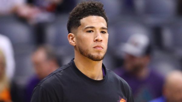 Devin Booker looks on wearing a Suns warmup shirt