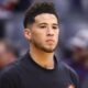 Devin Booker looks on wearing a Suns warmup shirt