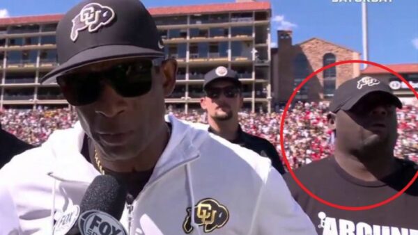Deion Sanders being interviewed with his bodyguard in the background