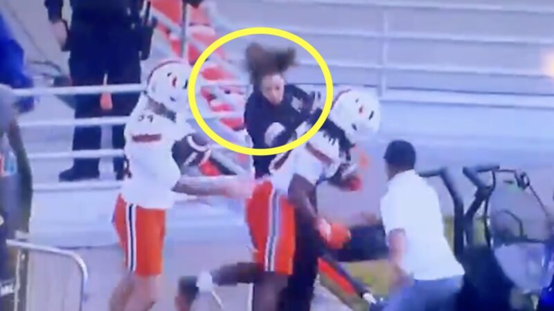 A woman is bulldozed by a Miami player on the sideline