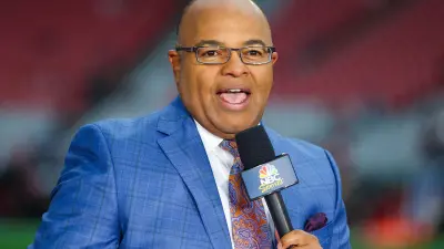 Mike Tirico holds a microphone