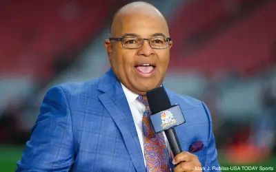 Mike Tirico holds a microphone